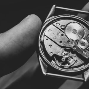 Black and white close-up of a vintage watch mechanism held in hand, showcasing intricate gears.
