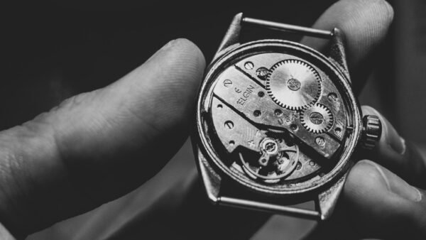 Black and white close-up of a vintage watch mechanism held in hand, showcasing intricate gears.