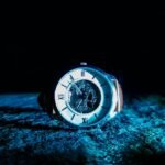 Close-up of a mechanical watch with Roman numerals, illuminated in dramatic lighting.